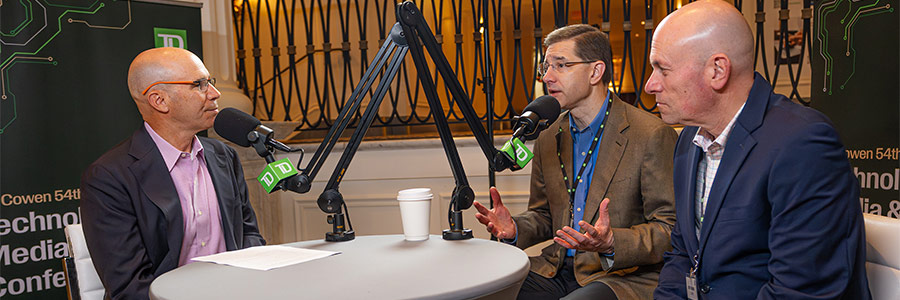 Three people seated around a table speaking into TD-branded microphones during a recorded discussion.