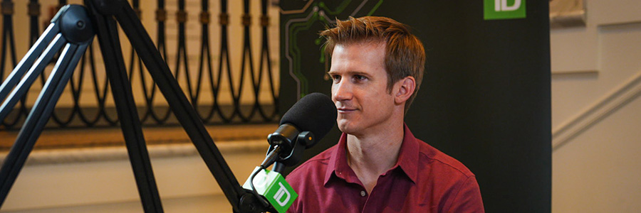 Person speaking into a microphone during a recorded interview, TD logo visible in background.
