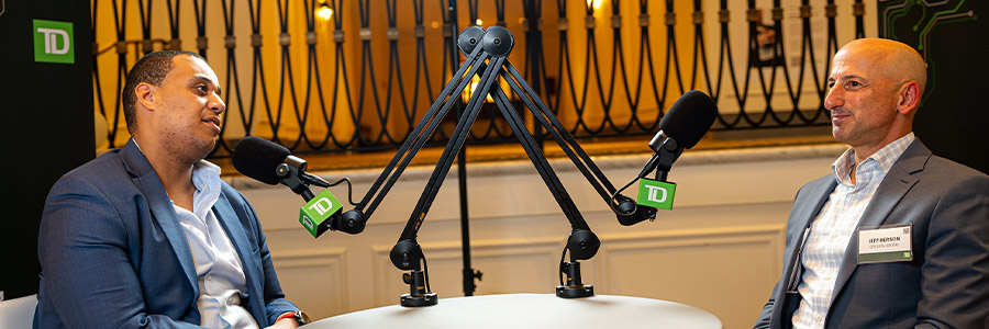 Two speakers seated across from each other with TD-branded microphones during a recorded discussion at an event.