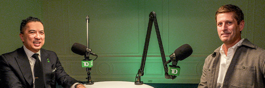 Two people seated at a small table with TD?branded microphones in a recording studio.