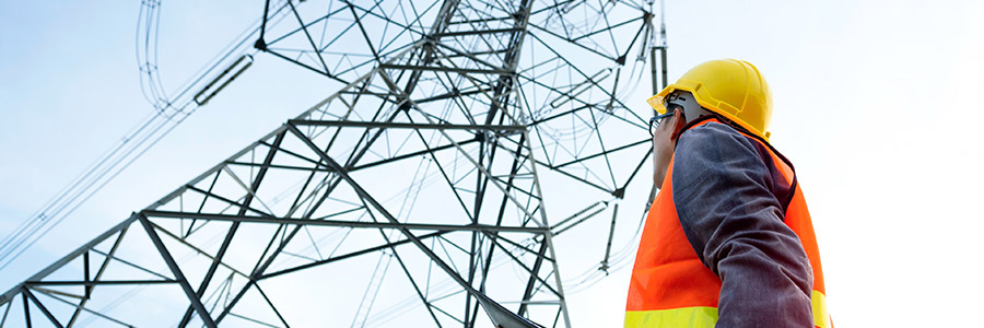 Utilities worker looking up at a high voltage tower