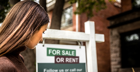 Woman looking over at a house for-sale or rent sign