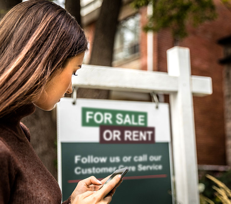 Woman looking over at a house for-sale or rent sign