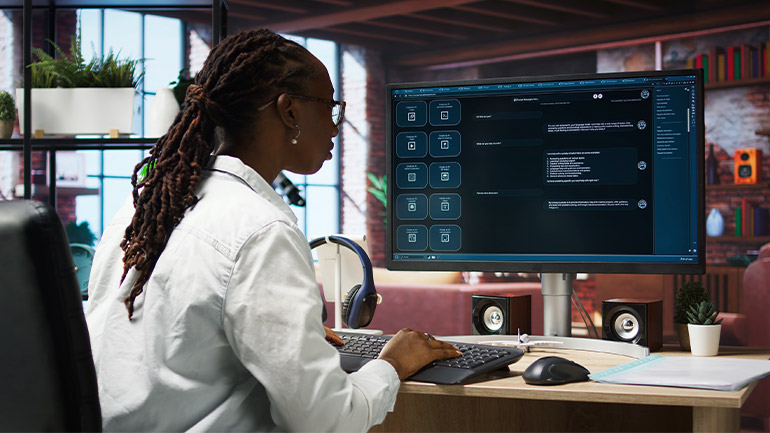 Personne travaillant sur un ordinateur de bureau dans un bureau moderne, utilisant un grand écran affichant une interface de clavardage avec de multiples fenêtres de conversation.