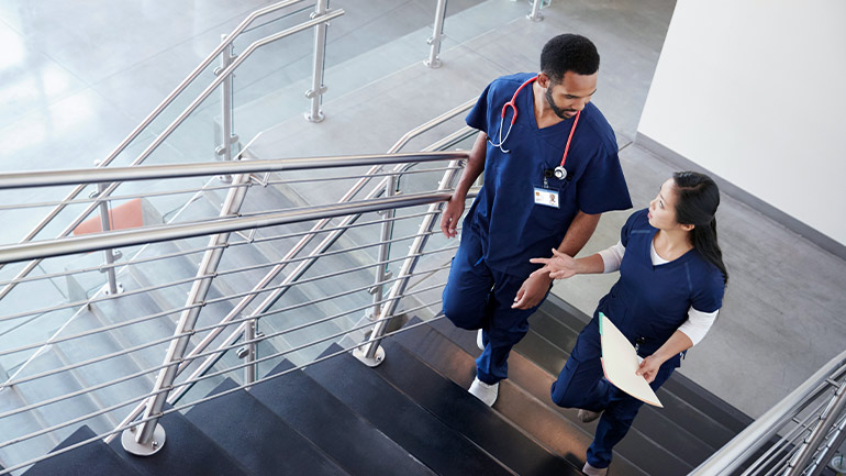 Two medical professionals ascend a stairway in an office building while conversing.