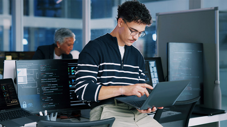 Person working on a laptop in a modern office with multiple monitors displaying code.