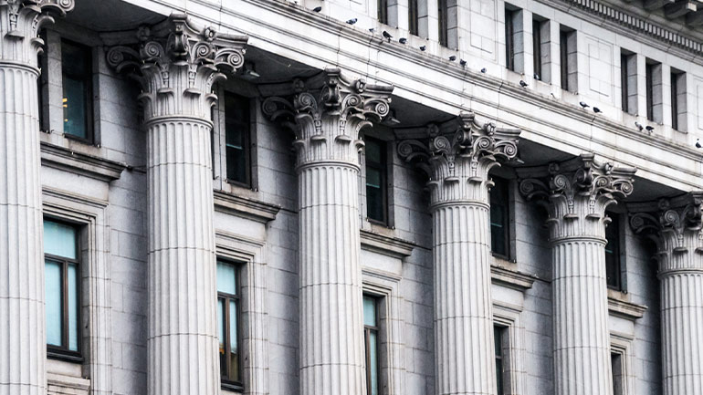 Row of classical stone columns with ornate capitals on a historic building façade.