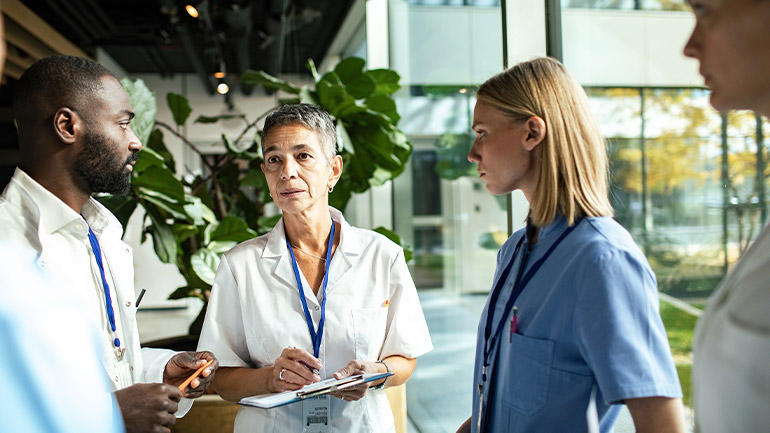 Healthcare professionals in discussion, reviewing notes in a bright clinic or hospital setting.