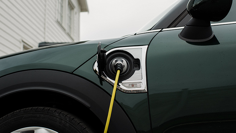 Electric car charging cable plugged into an electric vehicle’s side port outside a suburban house.
