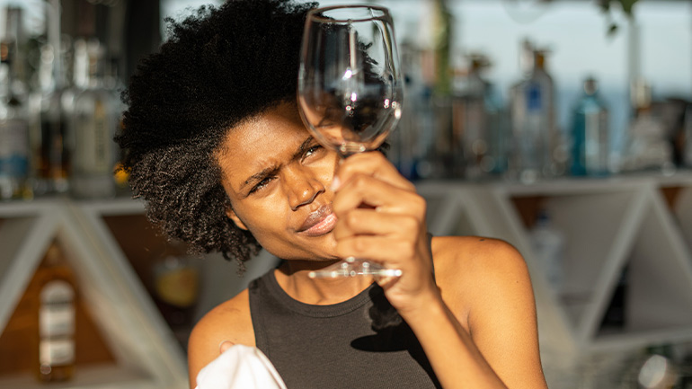 Person inspecting an empty wine glass in a bar setting, with bottles blurred in the background.