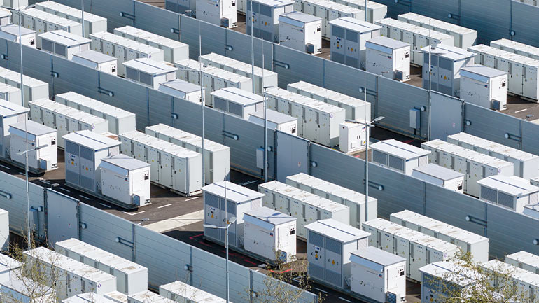Rows of industrial battery storage units arranged in a grid at a power facility.