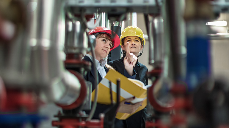 Two professionals in hardhats examine machinery.