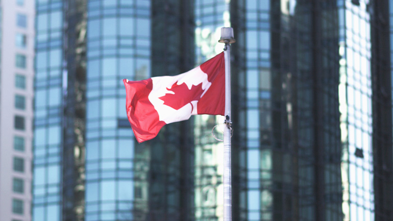 Canadian flag flying in front of downtown office towers.