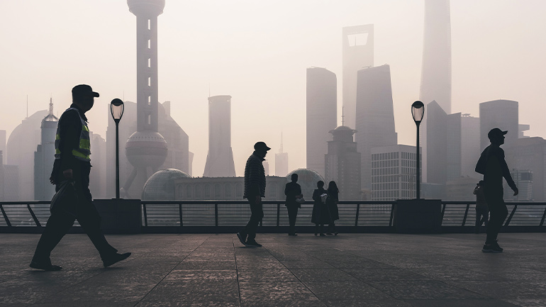 Pedestrians walking along Shanghai waterfront with city skyline in haze.
