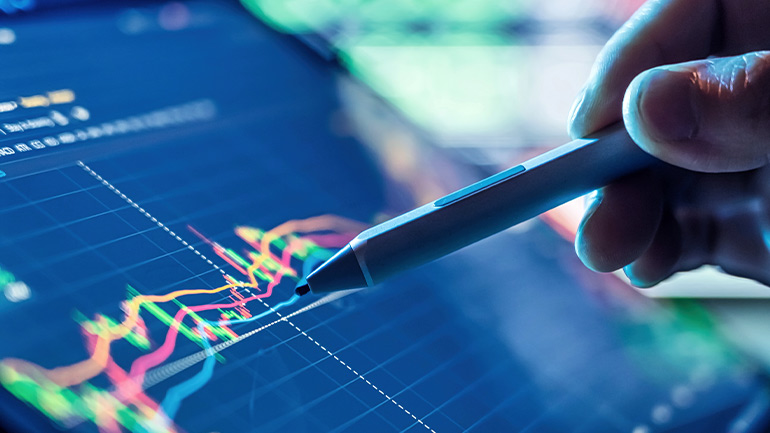 Une main tenant un stylet et pointant un écran numérique affichant des graphiques financiers colorés.
