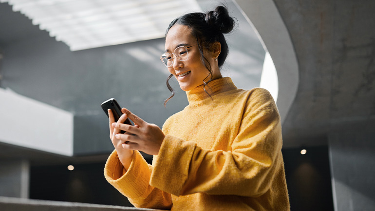 Person in a yellow sweater smiling while using a smartphone in a modern concrete interior.