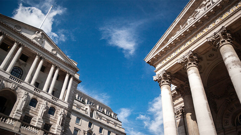 The Bank of England building facing the Royal Exchange under a blue sky.