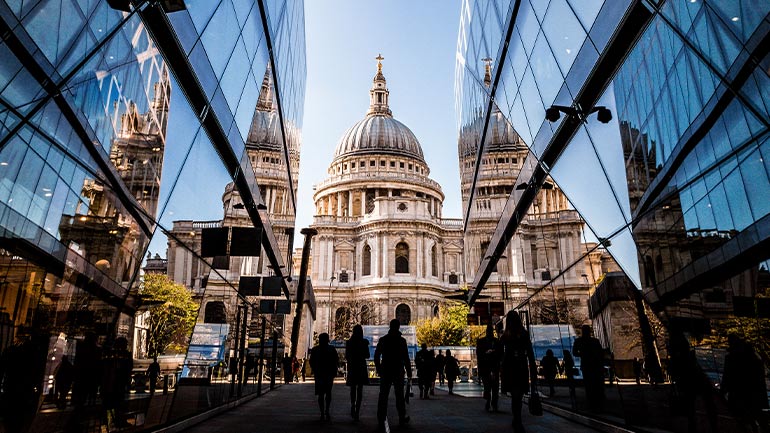 St. Paul’s Cathedral in London viewed between modern glass buildings with people walking in the foreground.
