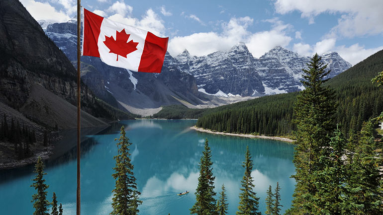 Un drapeau canadien qui flotte à l’avant-plan d’un paysage montagneux