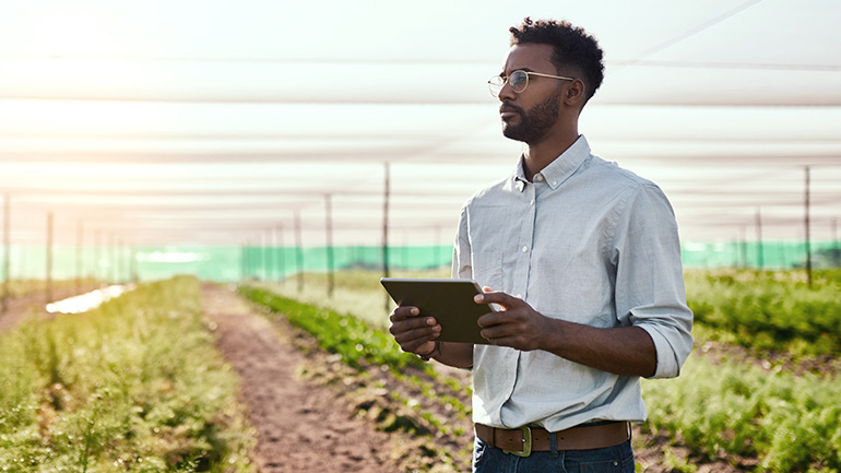 A man holding a tablet computer while inside a greenhouse.