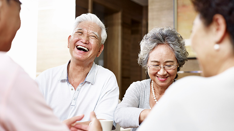 An elderly couple smiles and laughs with friends