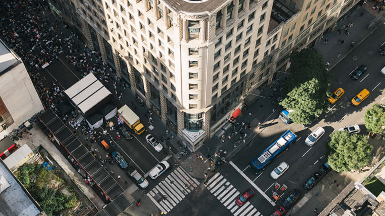 Aerial view of a busy downtown intersection with traffic, pedestrians, and surrounding city buildings.