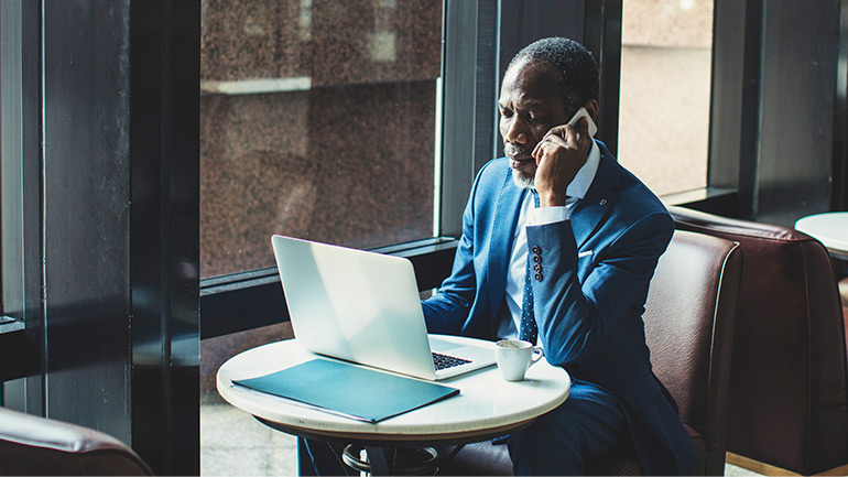 A professional stares at a laptop screen while taking a mobile call. 