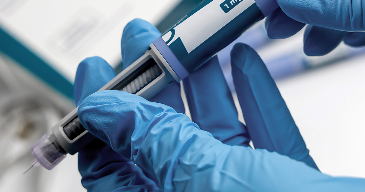 Close-up of latex gloved hands holding an insulin pen injector.