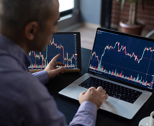 A person is looking at charts on two computer screens and comparing data.