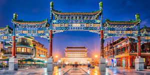 Ornate traditional Chinese gate at night with city buildings in the background.
