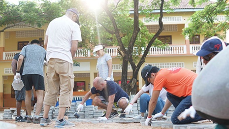 People working together outdoors, arranging paving stones in front of a building.